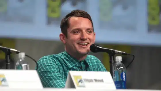 Elijah Wood speaking into a microphone at San Diego Comic-Con in 2014; archive photograph with AI-assisted landscape adaptation