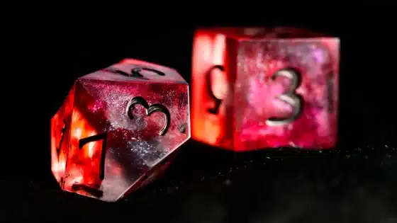A red glittering ten-sided resin die beside a red six-sided die against a dark background